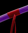 Purple katana scabbard with gold cap, red cord wrap, and floral emblem, on black background.