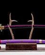 Purple-bladed handmade anime katana with gold accents on display stand, decorative sheath below.